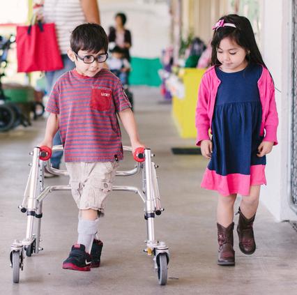 Visually impaired boy with walker walks with girl